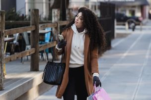 Attentive female carrying shopping bags while walking with smartphone